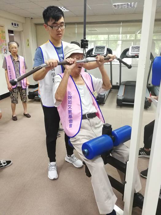 志工同學協助阿公使用滑輪下拉機，鍛鍊背部及上背部肌群
