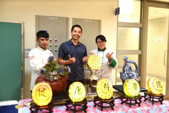 食科系呂哲維老師(中)帶領指導學生林尚汶同學(左)現場展示果雕作品